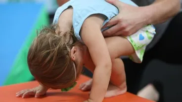A One Pea gymnast being spotted through a forward roll at Cal Elite