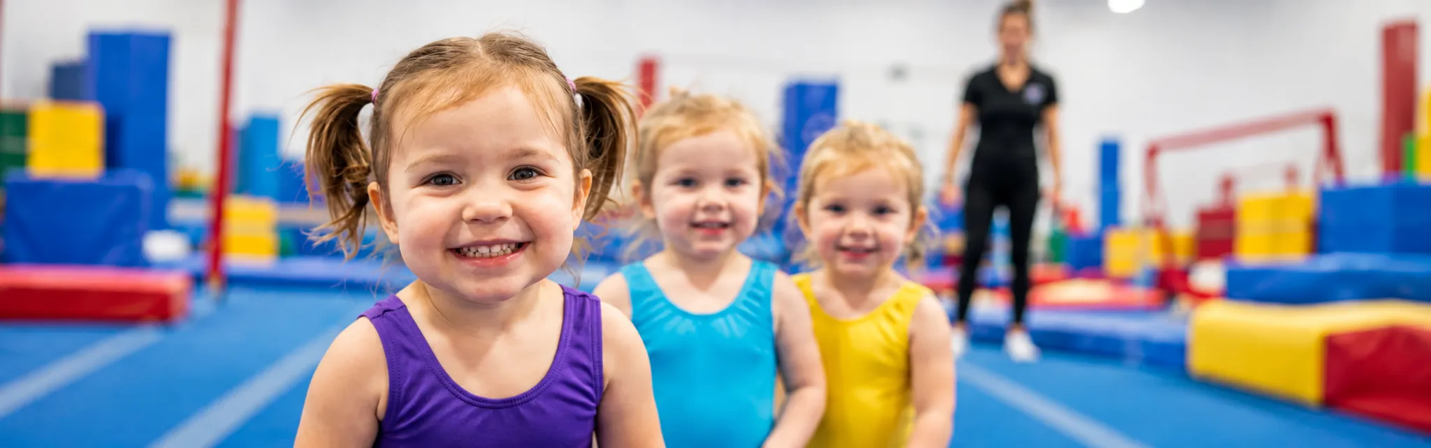 Three young gymnasts smiling together in the gym