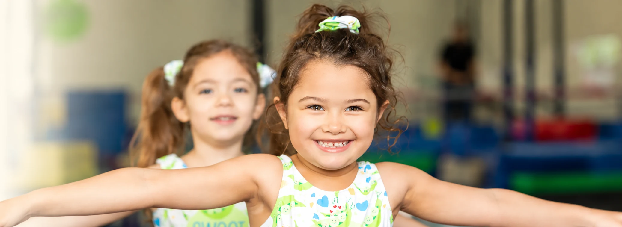 Two preschool gymnasts smiling with their arms outstretched